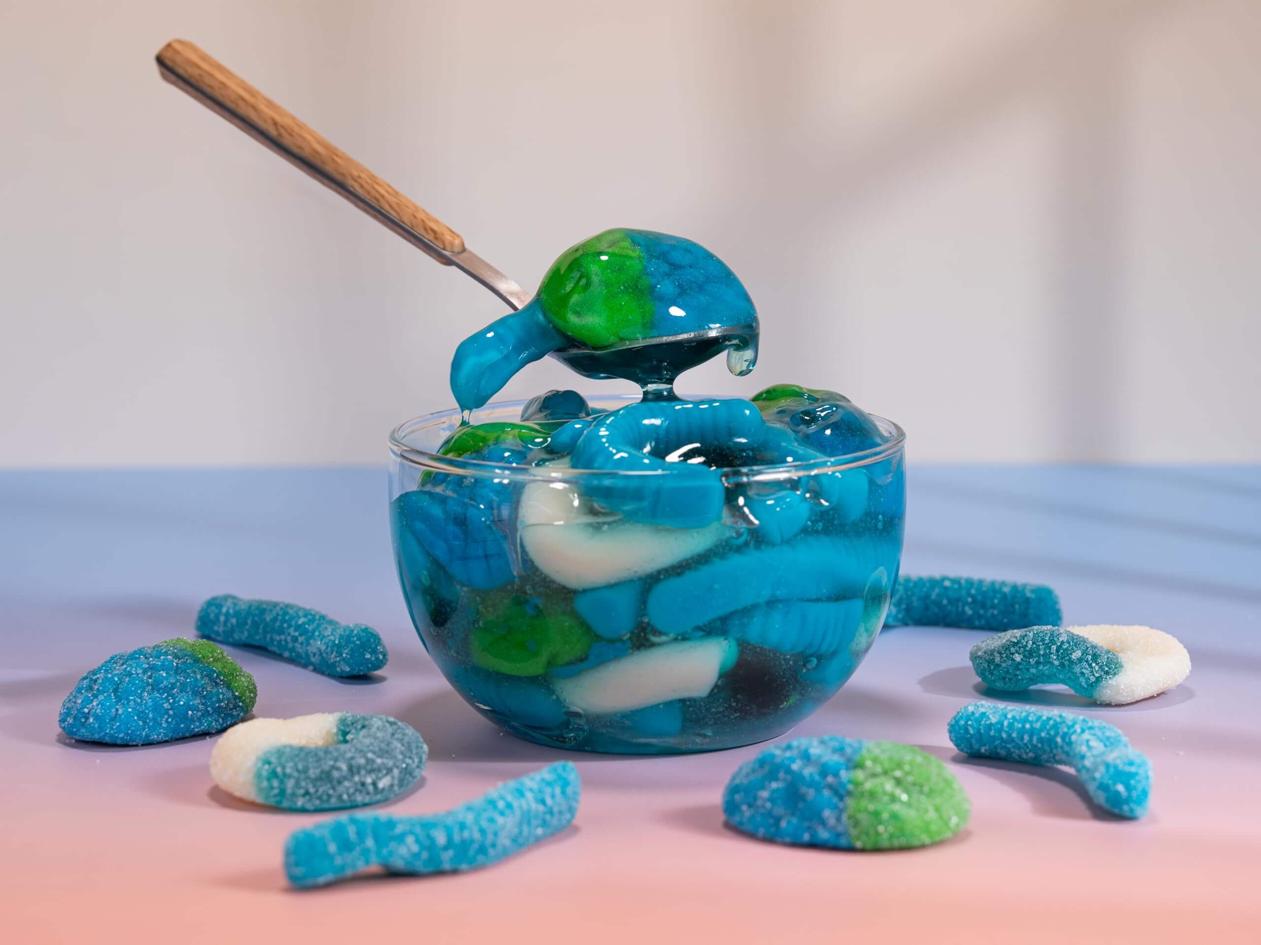 Viral Sour Gooey Gummies in a clear bowl with blue and green gummies and a wooden spoon, perfect for candy lovers.