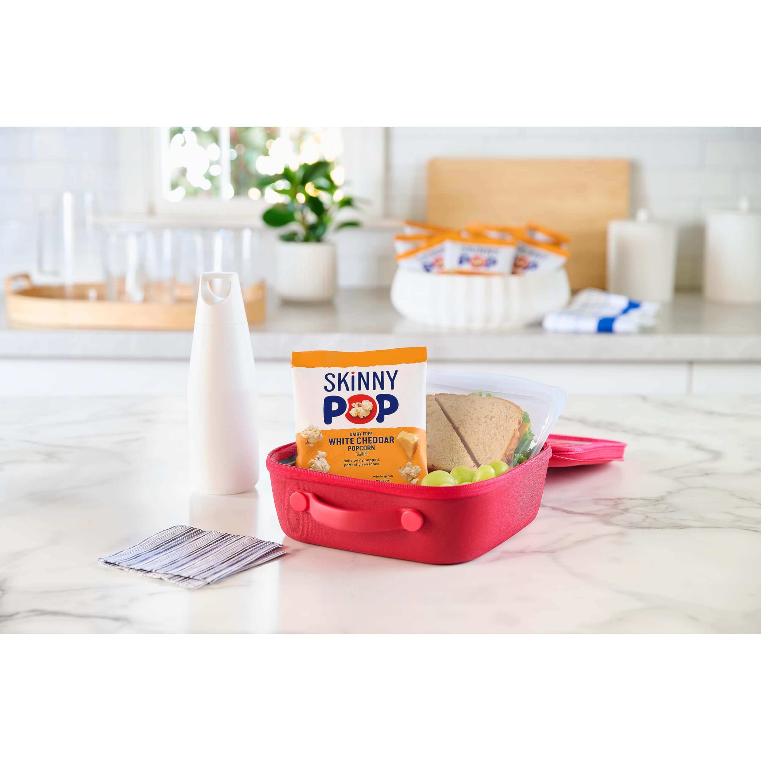 SkinnyPop Family Favorite Variety Pack placed in a vibrant snack container on a kitchen countertop.