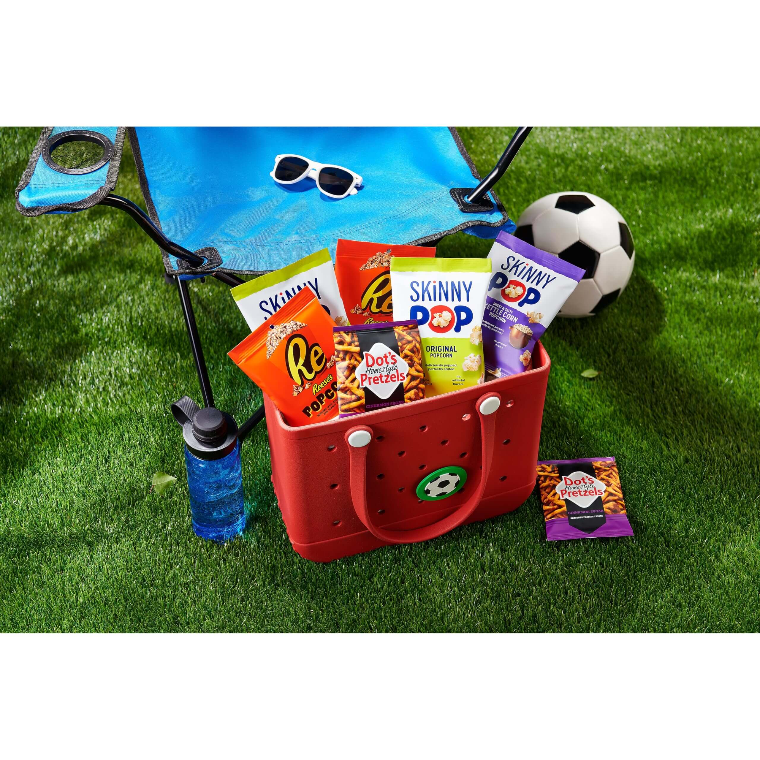 SkinnyPop Family Favorite Variety Pack in a colorful basket on grass with snacks and a soccer ball.