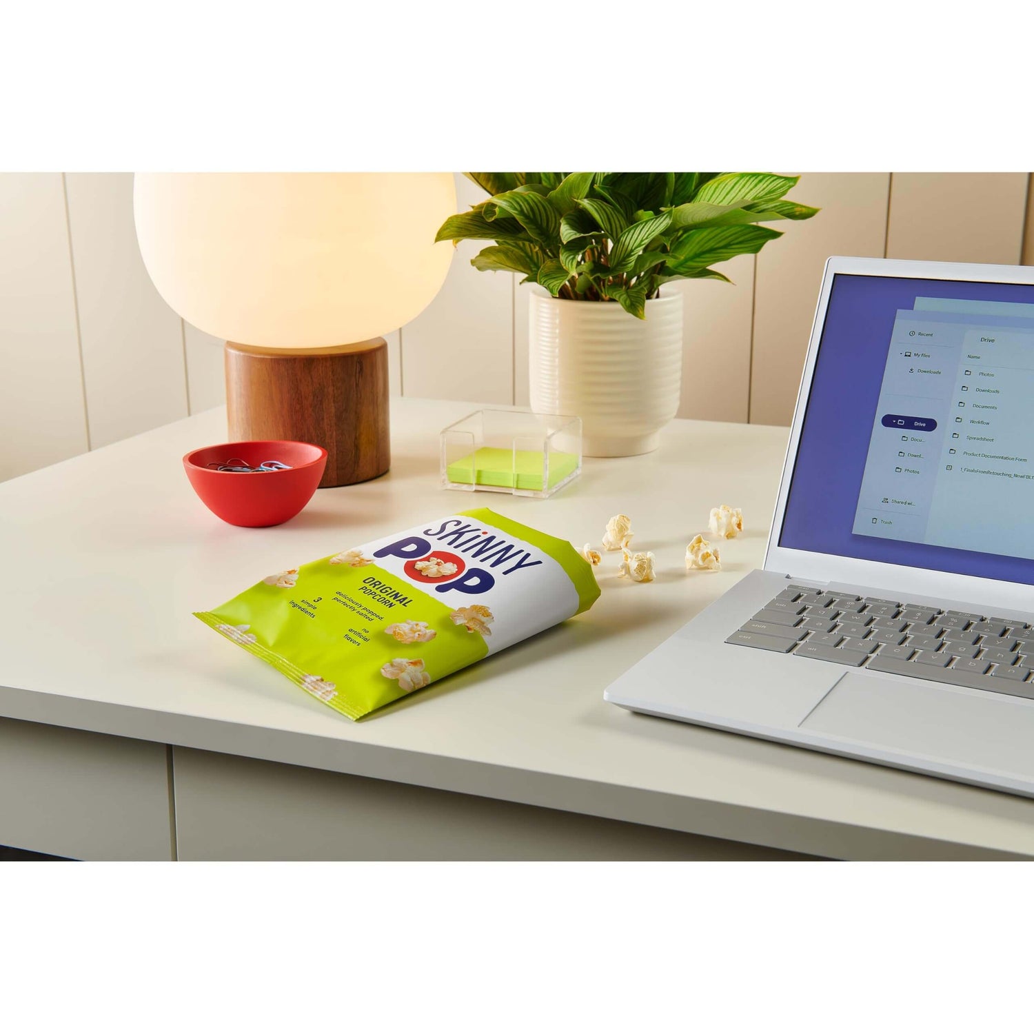 SkinnyPop Family Favorite Variety Pack on a desk next to a laptop and a lamp, ideal for snacking.