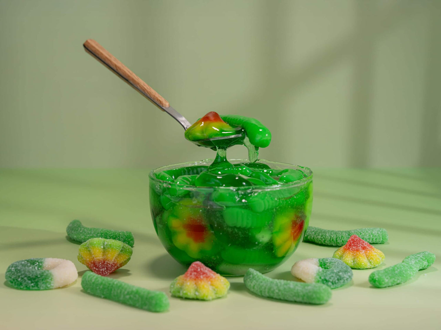 Viral Sour Gooey gummies in a green bowl with a wooden spoon, showcasing colorful chewy candies on a light green background.