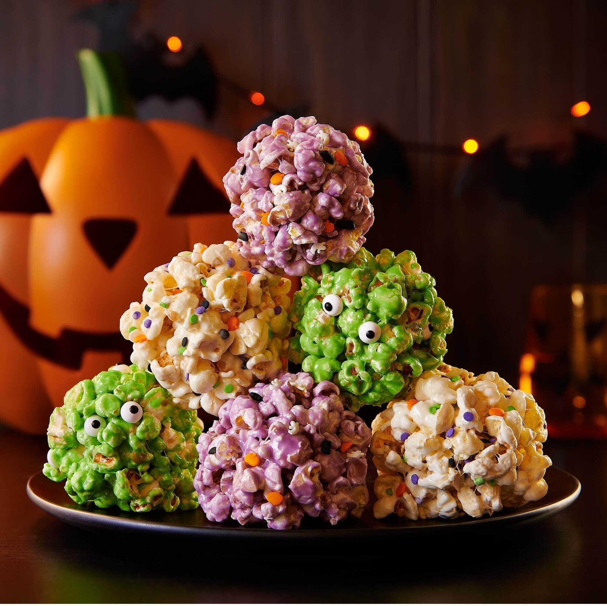 Colorful popcorn balls in Halloween shapes with a pumpkin in the background, perfect for celebrations.