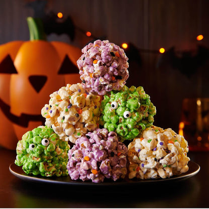 Colorful popcorn balls in Halloween shapes with a pumpkin in the background, perfect for celebrations.