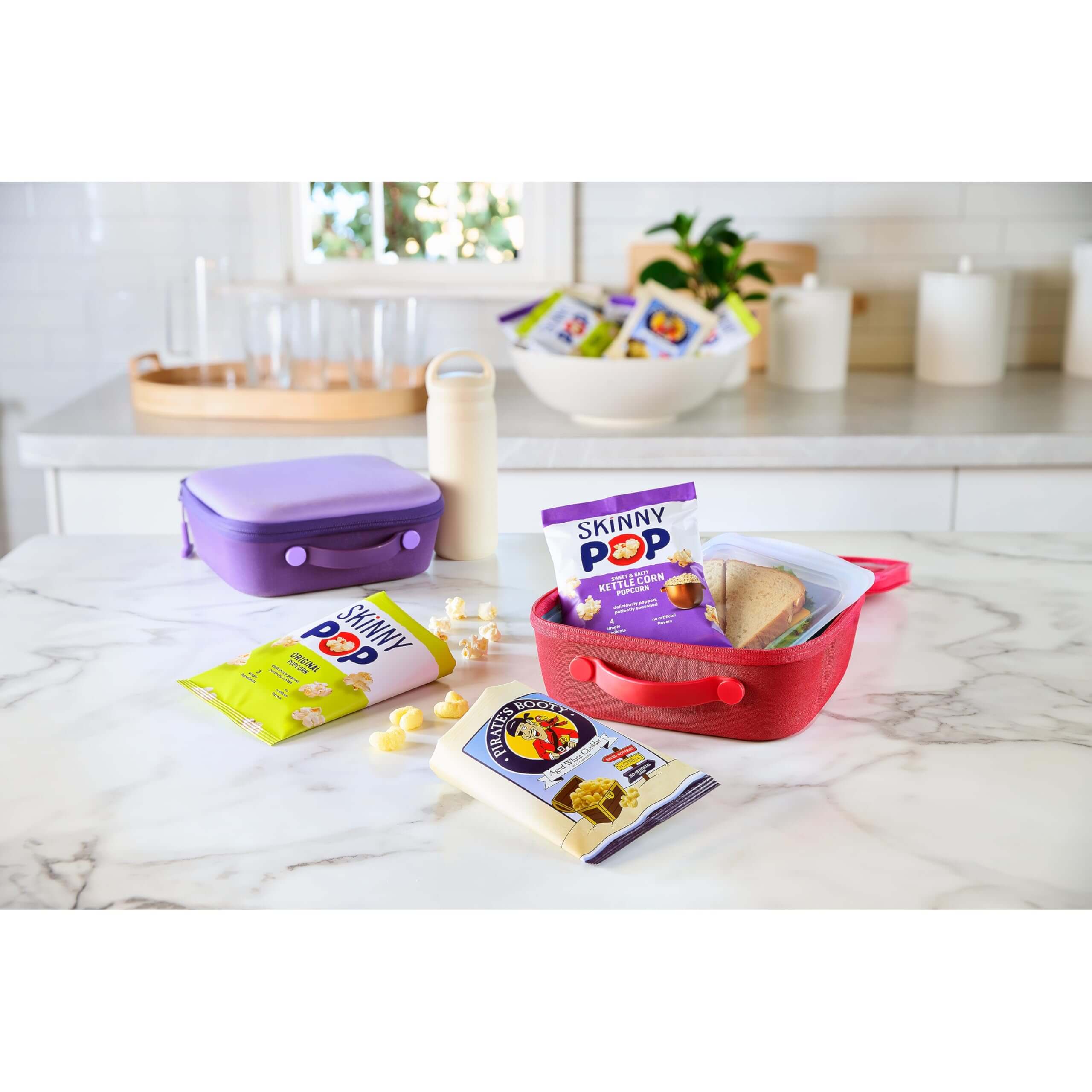 SkinnyPop Family Favorite Variety Pack with snacks in colorful containers on a kitchen counter.
